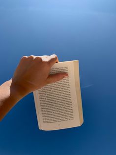 a hand holding an open book in front of a blue sky with the sun shining on it