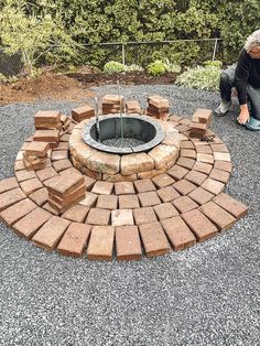 a man kneeling down next to a fire pit made out of bricks and brick blocks