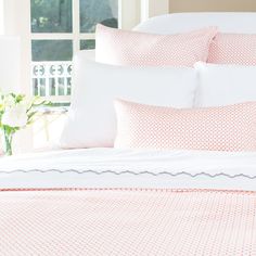 a bed with pink and white sheets, pillows and flowers on the headboard in front of a window