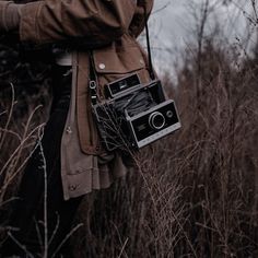 a woman holding an old fashioned camera in her hand while walking through tall grass and trees