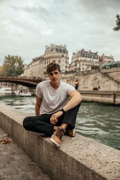 a young man sitting on the edge of a wall next to a body of water