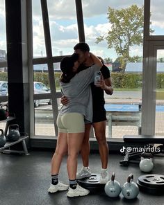 two people hugging each other while standing in front of a gym window with dumbbells on the floor