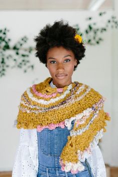 a woman with an afro is wearing a yellow scarf and denim overalls while standing in front of a white wall