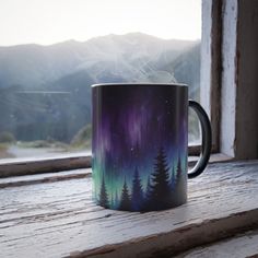 a coffee mug sitting on top of a window sill next to a forest filled with trees