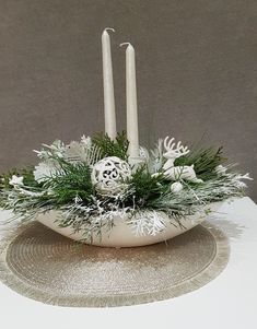 two candles are sitting in a white bowl with greenery and snowflakes on it