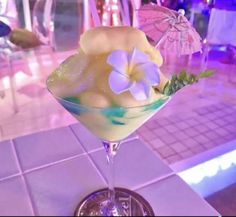 a drink in a martini glass with flowers and umbrellas on the table next to it