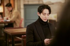 a man sitting at a table looking at his cell phone while wearing a black turtle neck sweater