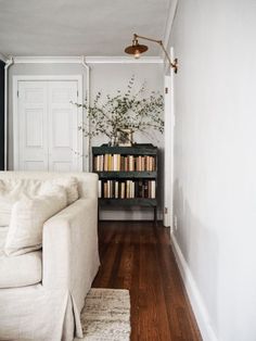 a living room with a white couch and bookshelf in the corner, next to a wooden floor