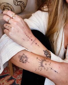 a woman sitting on the floor with her arm covered in stars and zodiac signs tattoo