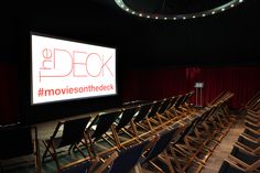 an empty auditorium with rows of chairs and a projector screen in the background that reads'the d c k movies on the deck '