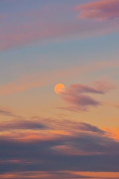 an airplane flying in the sky at sunset with a full moon behind it and some clouds