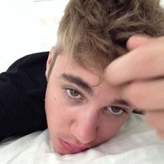 a young man laying on top of a bed holding his hand up to his head