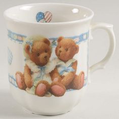 a coffee cup with two teddy bears on it's front and back sides, sitting next to each other