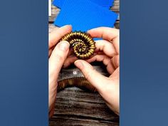 two hands are holding a piece of wood with a spiral design on it, while another hand holds a blue card