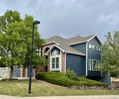 a blue house with trees and bushes on the front lawn in an upscale neighborhood setting