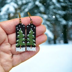 a pair of earrings with christmas trees on them in front of snow - covered trees