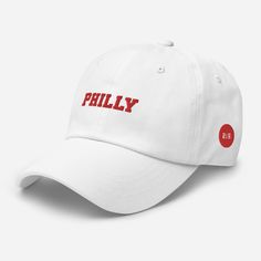 "Philly Embroidered Dad Hat with Red Text, Red and white Philly hat, Philadelphia hat, Philly ball cap, Cute Philly Hat An outfit paired with a dad hat just hits differently. A truly classic item that serves a fresh look any time of the day. * 100% chino cotton twill * Green Camo color is 35% chino cotton twill, 65% polyester * Unstructured, 6-panel, low-profile * 6 embroidered eyelets * 3 ⅛\" (7.6 cm) crown * Adjustable strap with antique buckle * Blank product sourced from Vietnam or Bangladesh This product is made especially for you as soon as you place an order, which is why it takes us a bit longer to deliver it to you. Making products on demand instead of in bulk helps reduce overproduction, so thank you for making thoughtful purchasing decisions!" White Snapback Visor Hat With Letter Print, White Letter Print Visor Snapback Hat, White Letter Print Snapback Visor Hat, White Snapback Hat With Curved Bill For Baseball Season, White Adjustable Fitted Hat With Embroidered Logo, White Trucker Hat With Letter Print Visor, Classic White Trucker Hat, White Curved Bill Hat For Baseball Season, White Hat With Letter Print, One Size