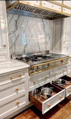 an open drawer in the middle of a kitchen with white cabinets and marble counter tops