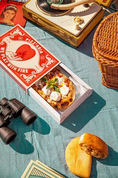 an open pizza box sitting on top of a table next to binoculars and other items