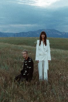 two people standing in a field with mountains in the background