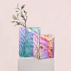 two square vases with flowers in them sitting on a white pedestal against a pink wall