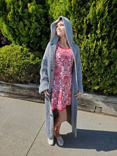 a woman in a red dress and gray cardigan is standing on the sidewalk with her eyes closed