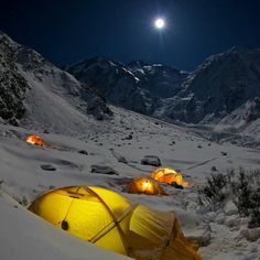 tents pitched up in the snow at night with mountains in the background and a full moon