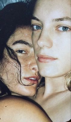 two women laying next to each other on top of a bed, one with blue eyes