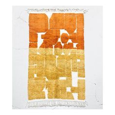 an orange and yellow rug with fringes on the bottom, in front of a white wall