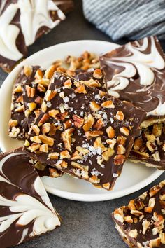 several pieces of chocolate barkle on a white plate with nuts and chopped walnuts