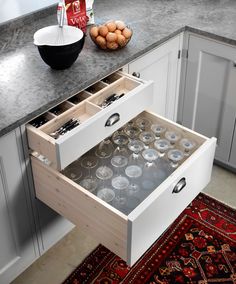 an open drawer in a kitchen next to a rug and bowl with eggs on it