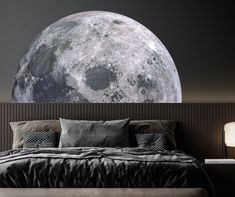 a bed with pillows and blankets in front of a large moon wall decal