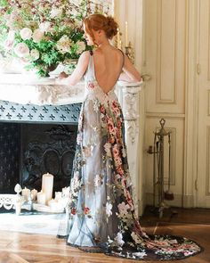 a woman standing in front of a fireplace wearing a dress with flowers on the back