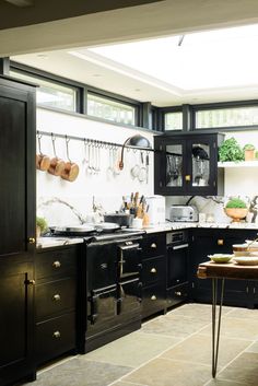 a kitchen with black cabinets and white walls has pots, pans, utensils hanging on the wall