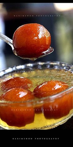 a spoon with some food in it on top of a glass bowl filled with liquid