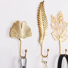 three gold leaf hooks hang on the wall next to black rubber cords and metal clips