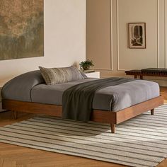 a bed sitting on top of a wooden floor next to a wall with paintings above it