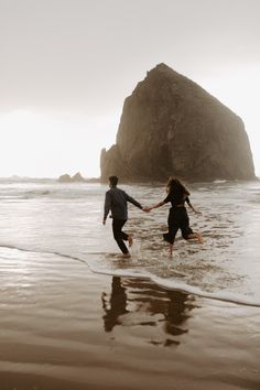 two people are running in the water at the beach with an island in the background