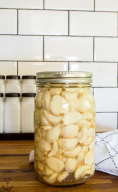 a jar filled with garlic sitting on top of a wooden table next to a white tile wall