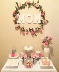 a table topped with cakes and cupcakes next to a mom's day sign