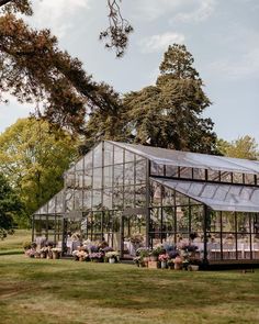 a group of people sitting in front of a large glass house on top of a lush green field