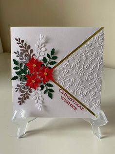 a christmas card with poinsettis and holly on it, sitting on a clear acrylic stand