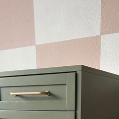 a green dresser sitting in front of a pink and white checkered wall with gold handles