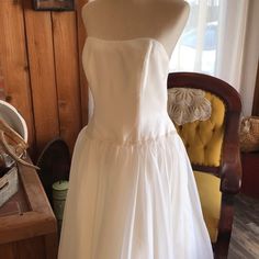 a white wedding dress on display in a room with a chair and other items around it