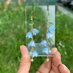 a pair of earrings with blue flowers and green leaves hanging from it's earwires