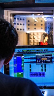 a man sitting in front of a computer monitor with sound mixing equipment on the screen