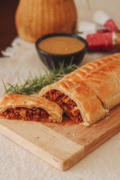 a meat filled pastry sitting on top of a wooden cutting board next to a bowl of dipping sauce