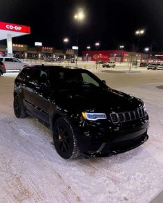 a black jeep parked in front of a gas station at night with snow on the ground