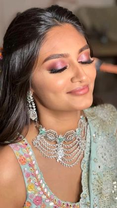 a woman with long dark hair wearing a blue dress and pink eyeshadow is smiling at the camera