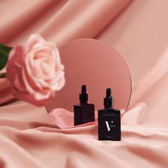 a bottle of perfume next to a mirror with a pink rose on the table behind it